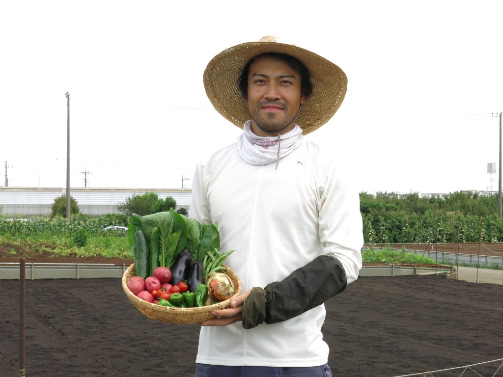 2015年の頃の栽培した野菜を持ち畑の前で記念撮影をする古川原琢さん
